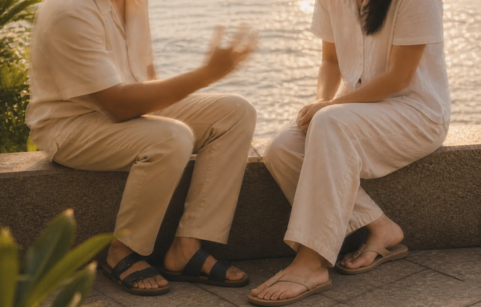 Two people talking with expressive hands beside tropical water.