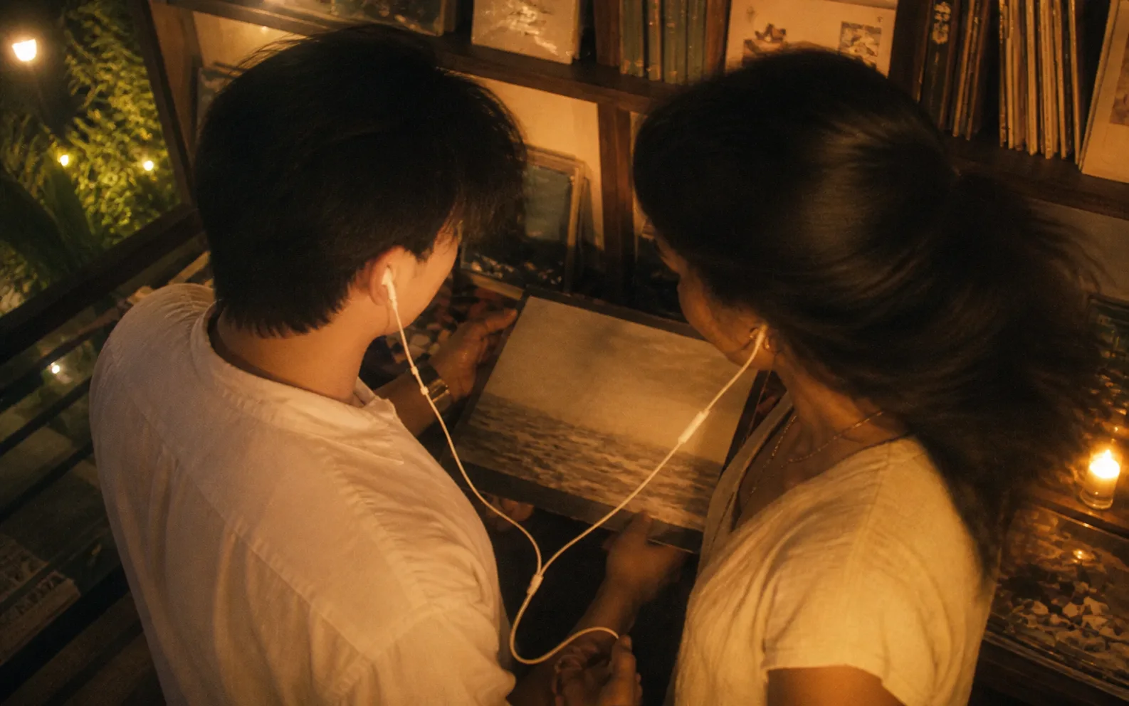 Two lightly dressed people sharing wired earphones in a warm record shop.